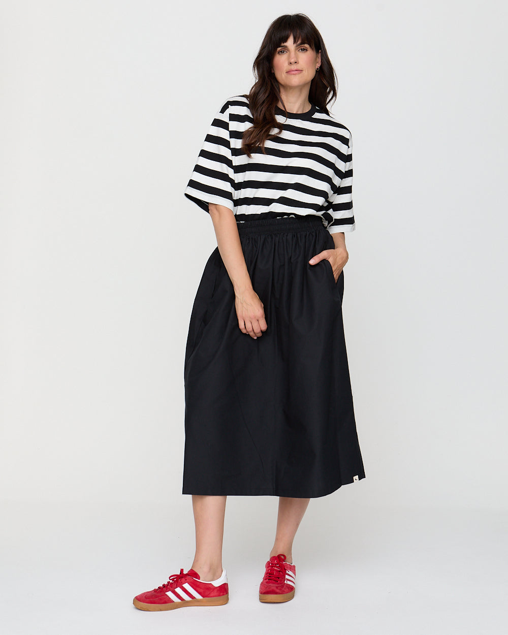 Woman wearing a black and white striped shirt, black skirt, and red sneakers on a white background
