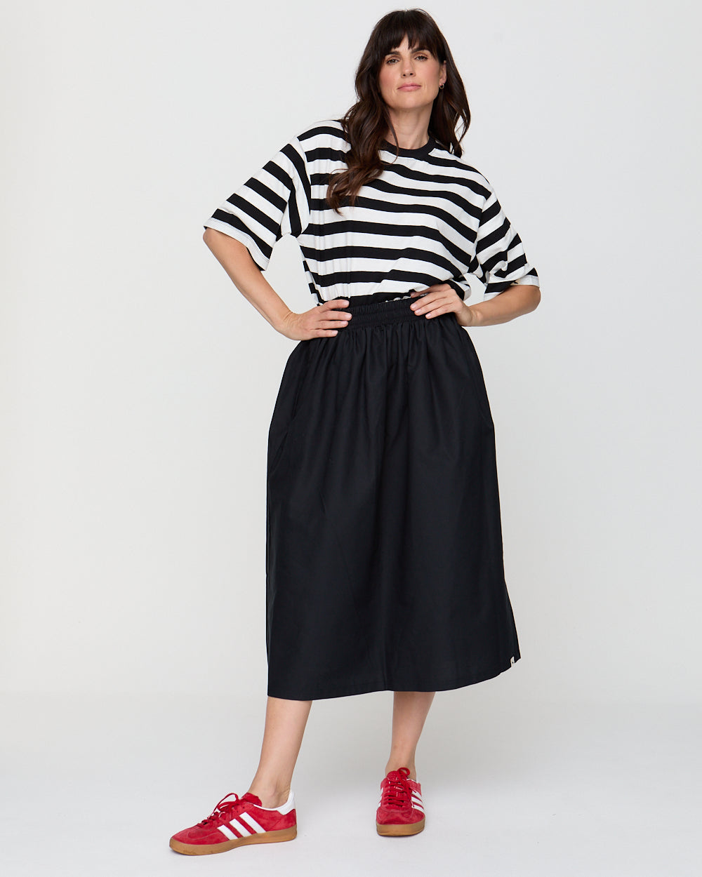 Woman wearing a black and white striped shirt and black skirt with red shoes on a white background