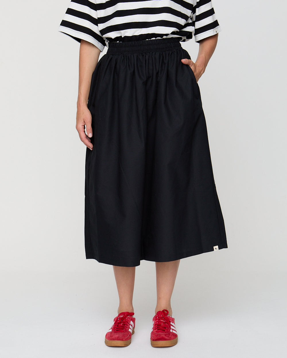Person wearing a black and white striped shirt, black skirt, and red sneakers on a white background