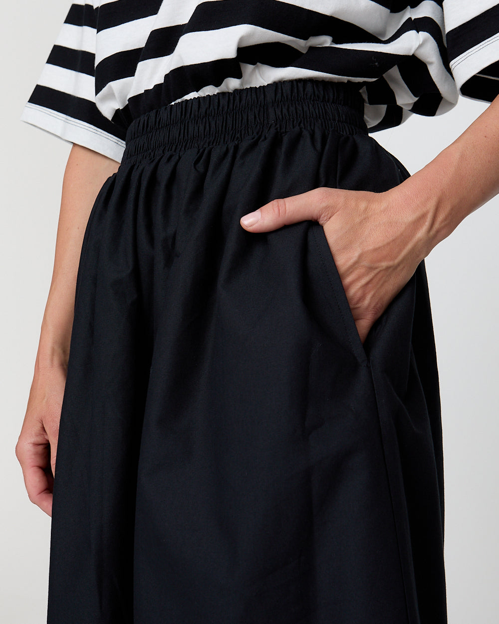 Person wearing a black skirt and black and white striped top on a white background