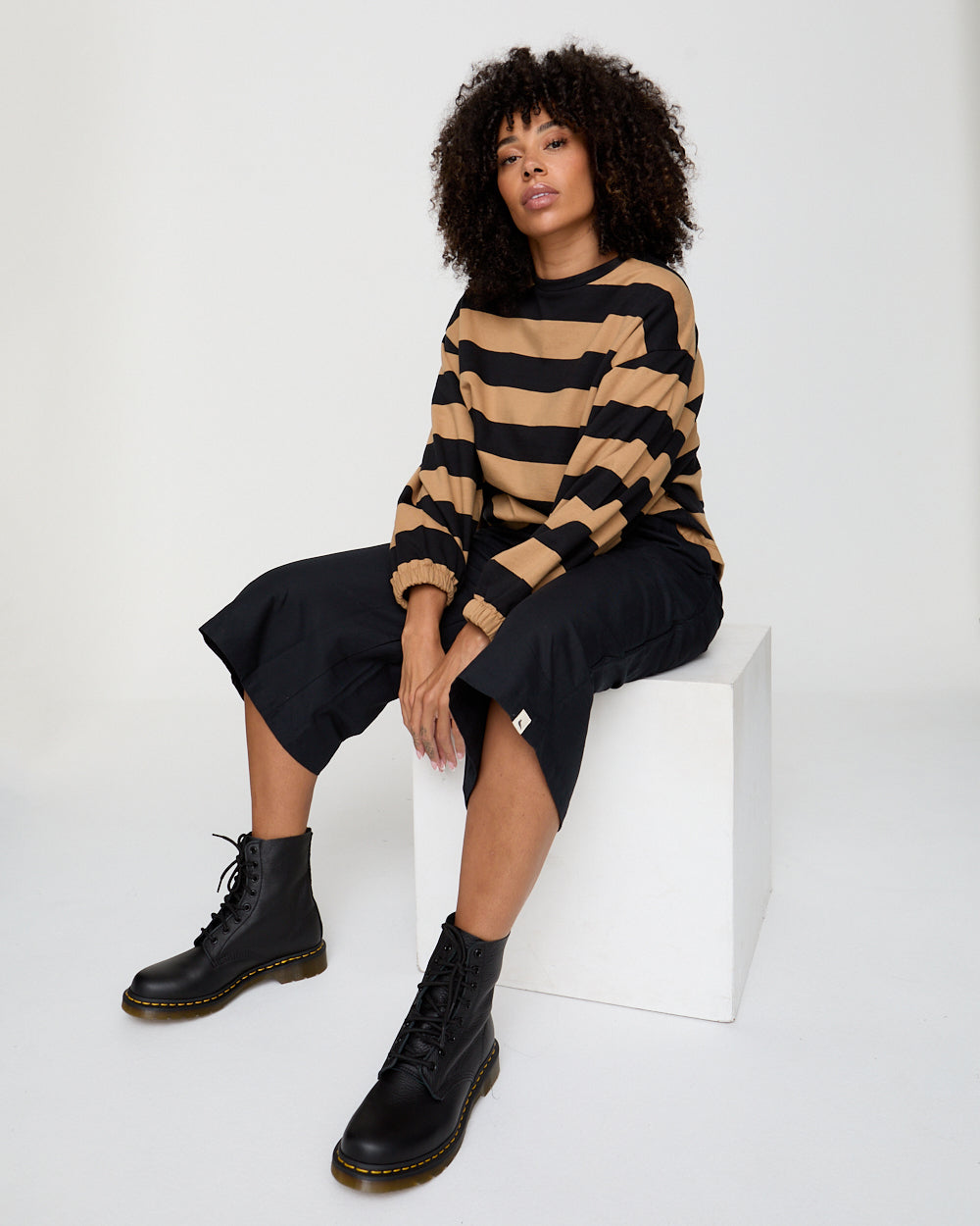 Person wearing a striped sweater and black boots sitting on a white block.
