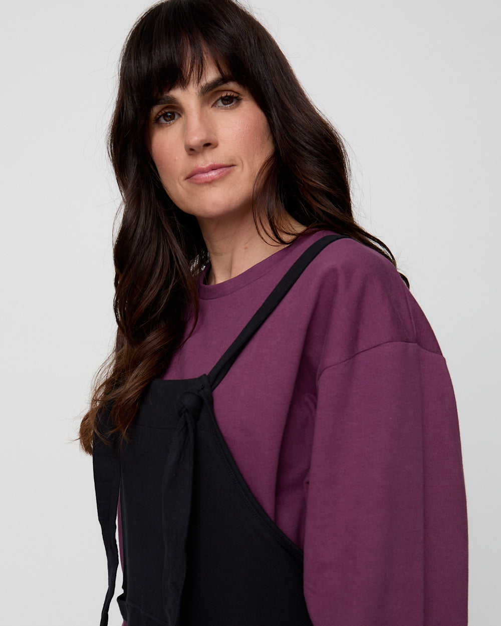 Woman wearing a purple sweatshirt with a black strap over her shoulder on a white background