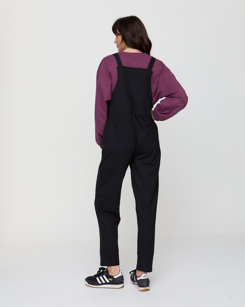 Person wearing black overalls and a purple shirt on a white background
