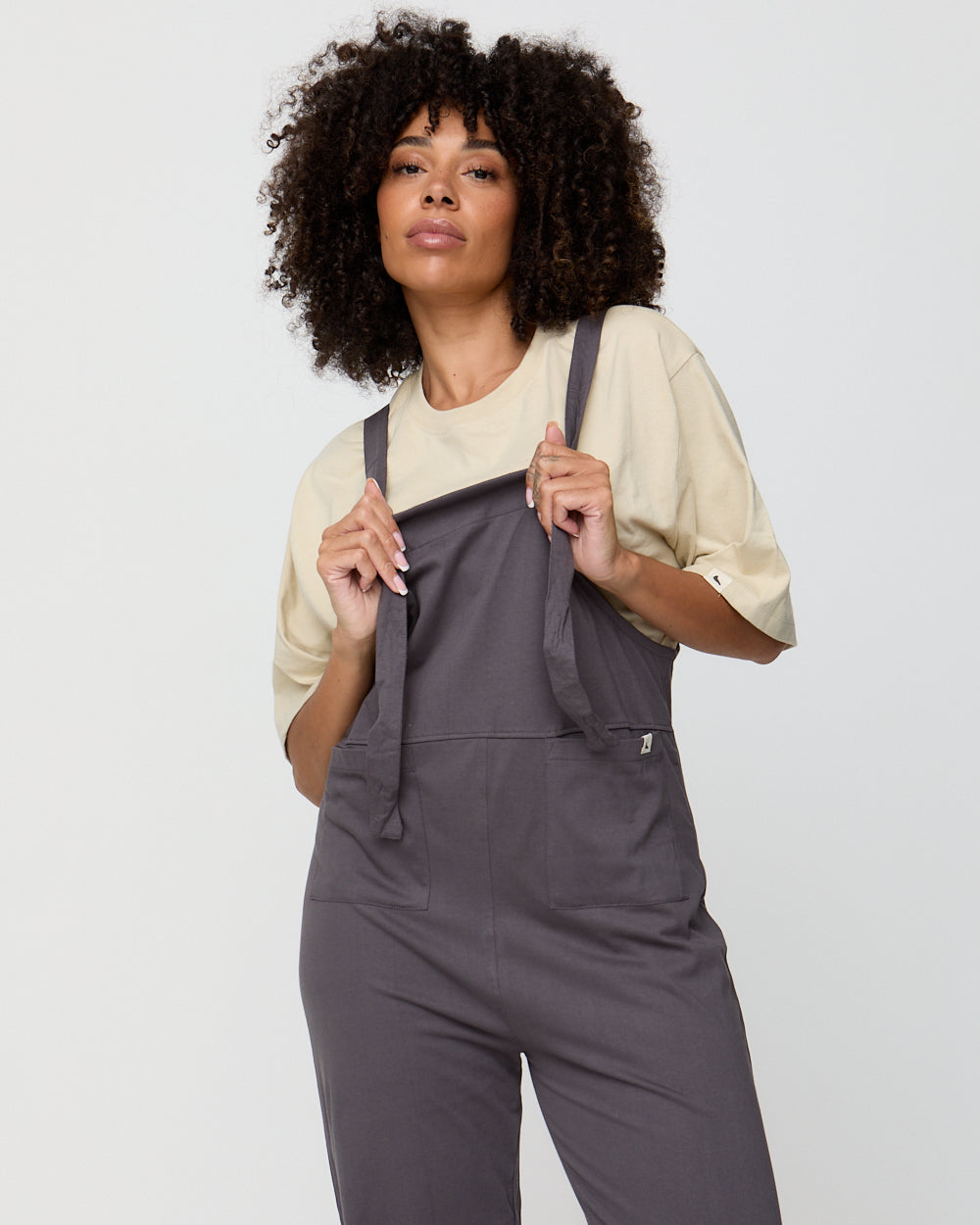 Woman wearing gray overalls against a plain background