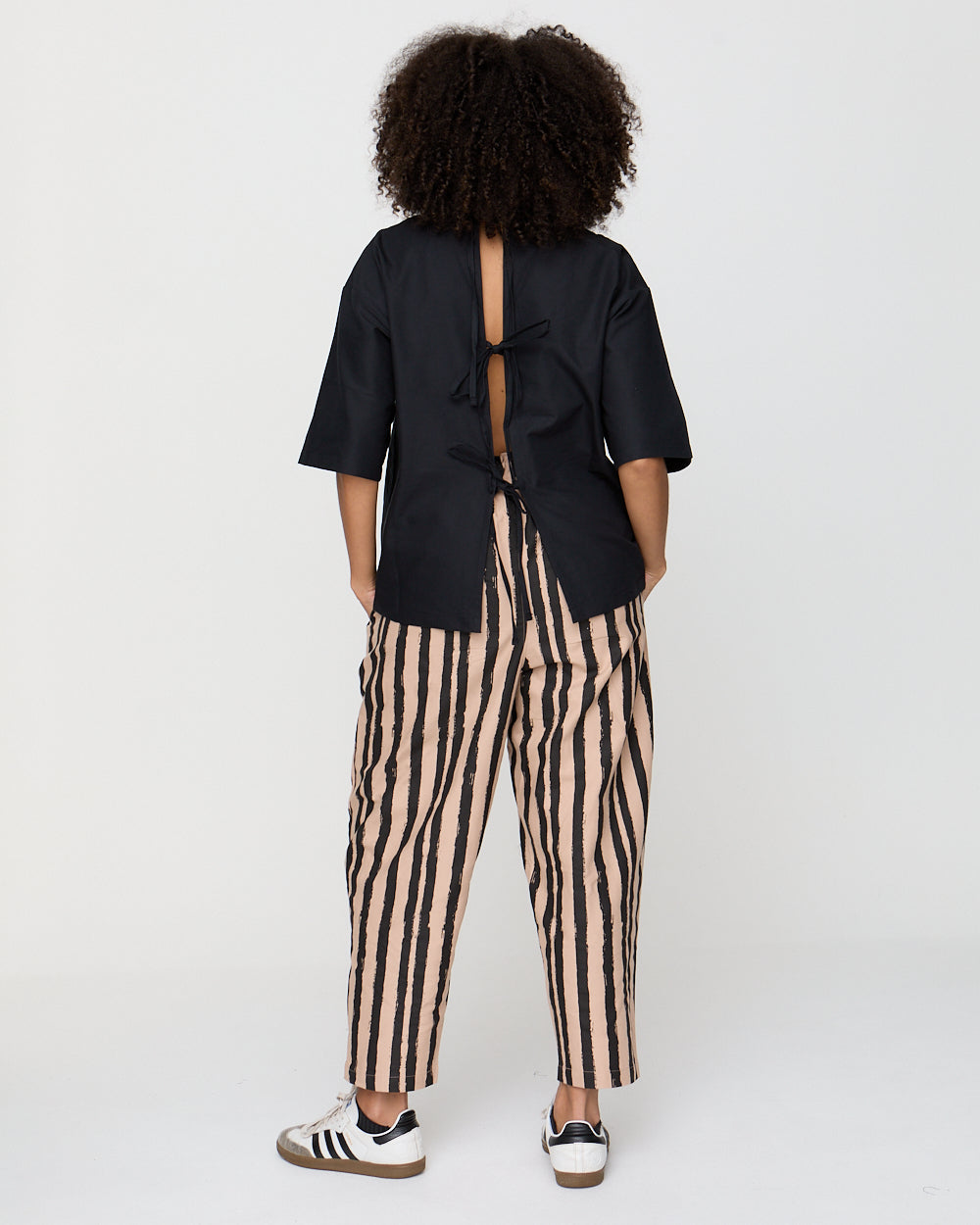 Person wearing a black open-back top and striped pants on a white background