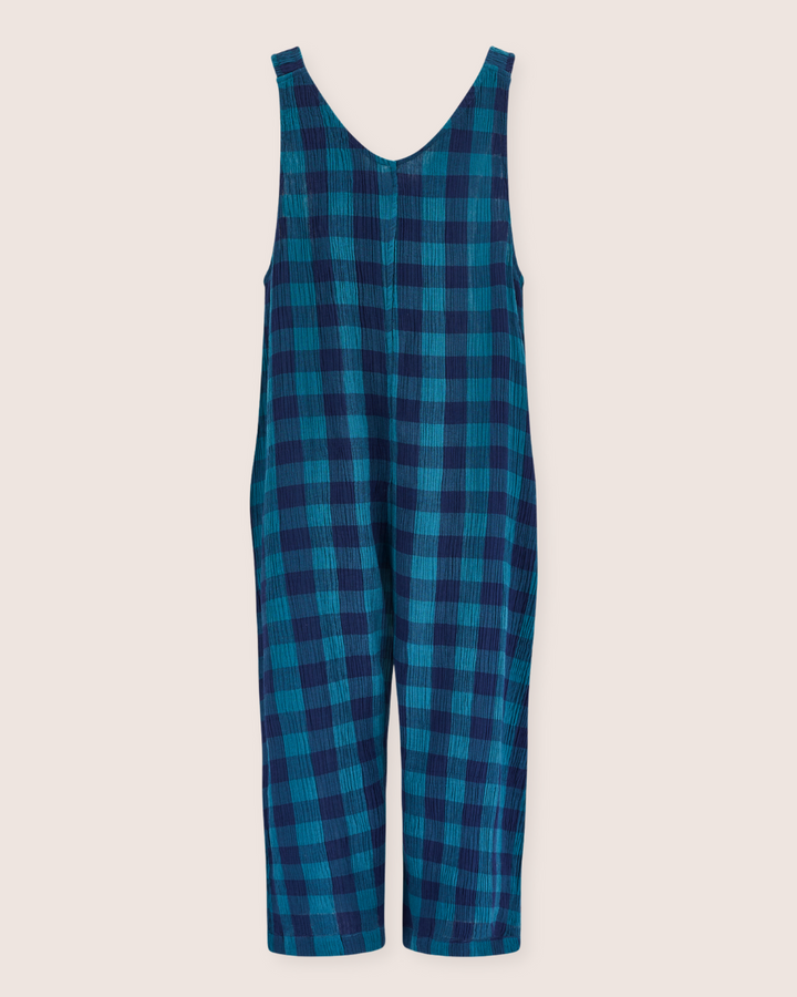 The Grace Check & Stripe Reversible Navy Jumpsuit, made of organic cotton, is sleeveless with blue and green checks. Its crinkled texture and wide legs make it a perfect sustainable wardrobe staple. It hangs against an off-white backdrop.