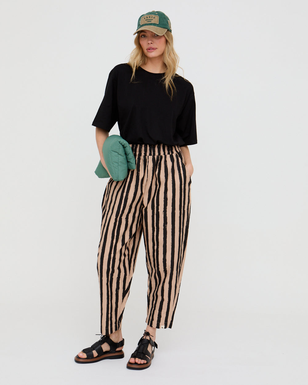 Kate painted stripe trouser - girl holds a green clutch wearing a cap 