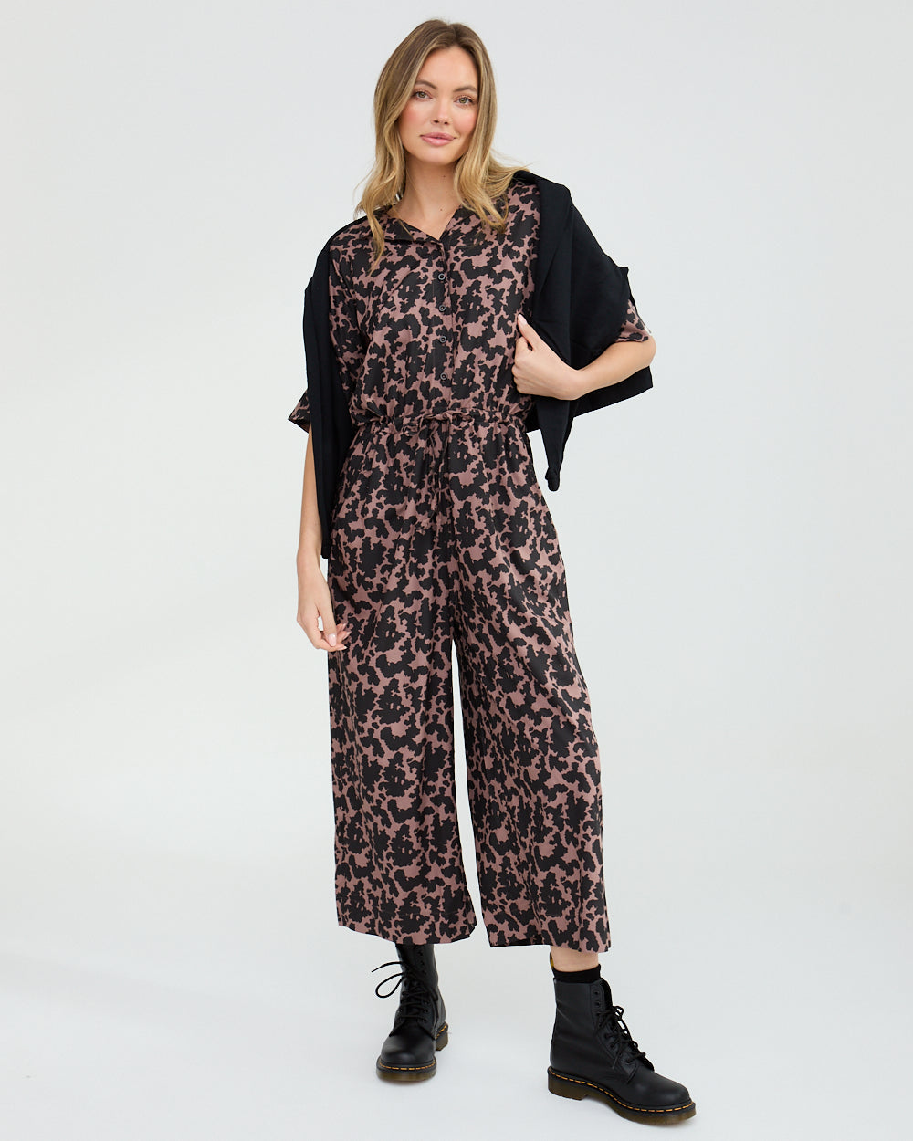 Woman wearing a leopard print jumpsuit with a black cardigan on a white background