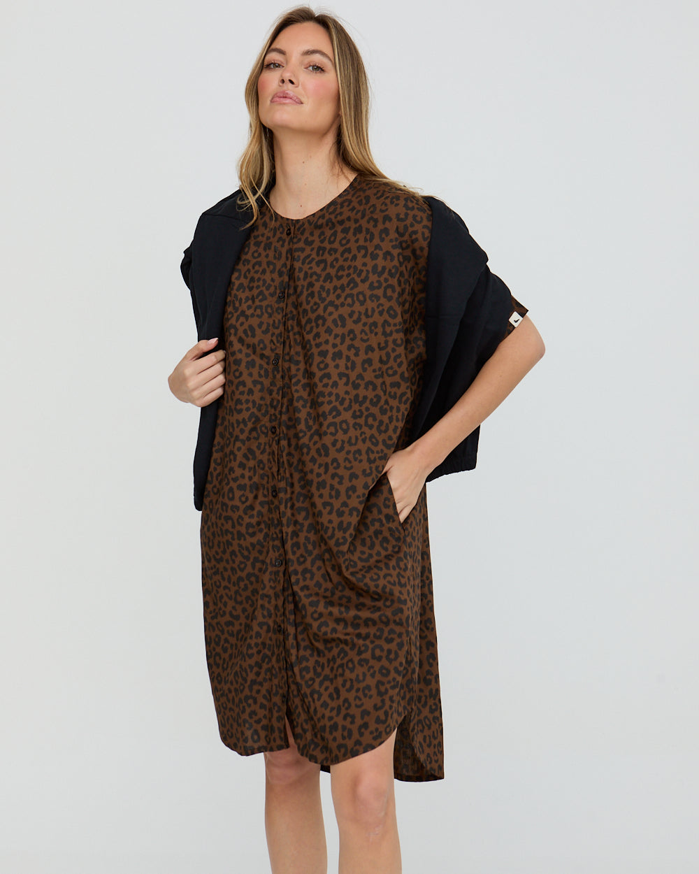 Woman wearing a leopard print dress with a black cardigan on a light gray background