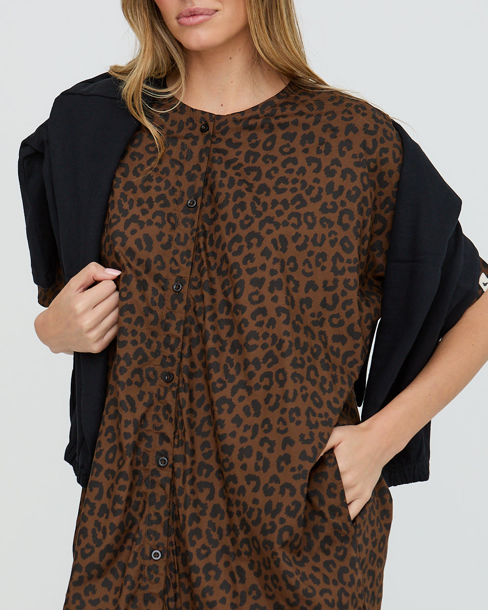 Woman wearing a brown leopard print dress with a black jacket over shoulders on a white background