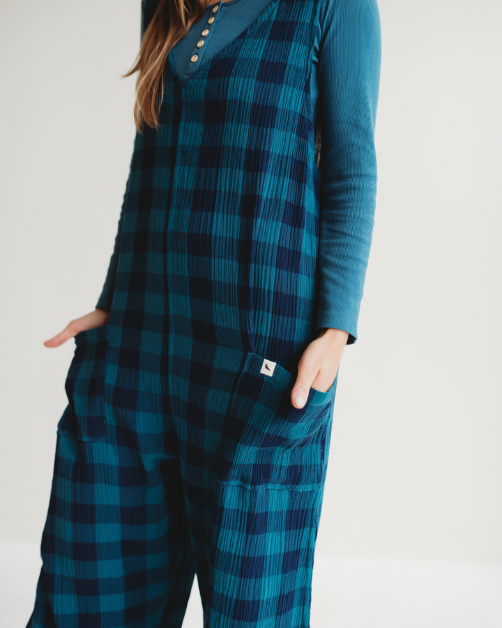 A person wearing a Grace Check & Stripe Reversible Navy Jumpsuit stands against a plain background. The matching long-sleeved top complements the jumpsuit, crafted from organic cotton. Its perfect for a sustainable wardrobe, with hands casually tucked into the pockets.