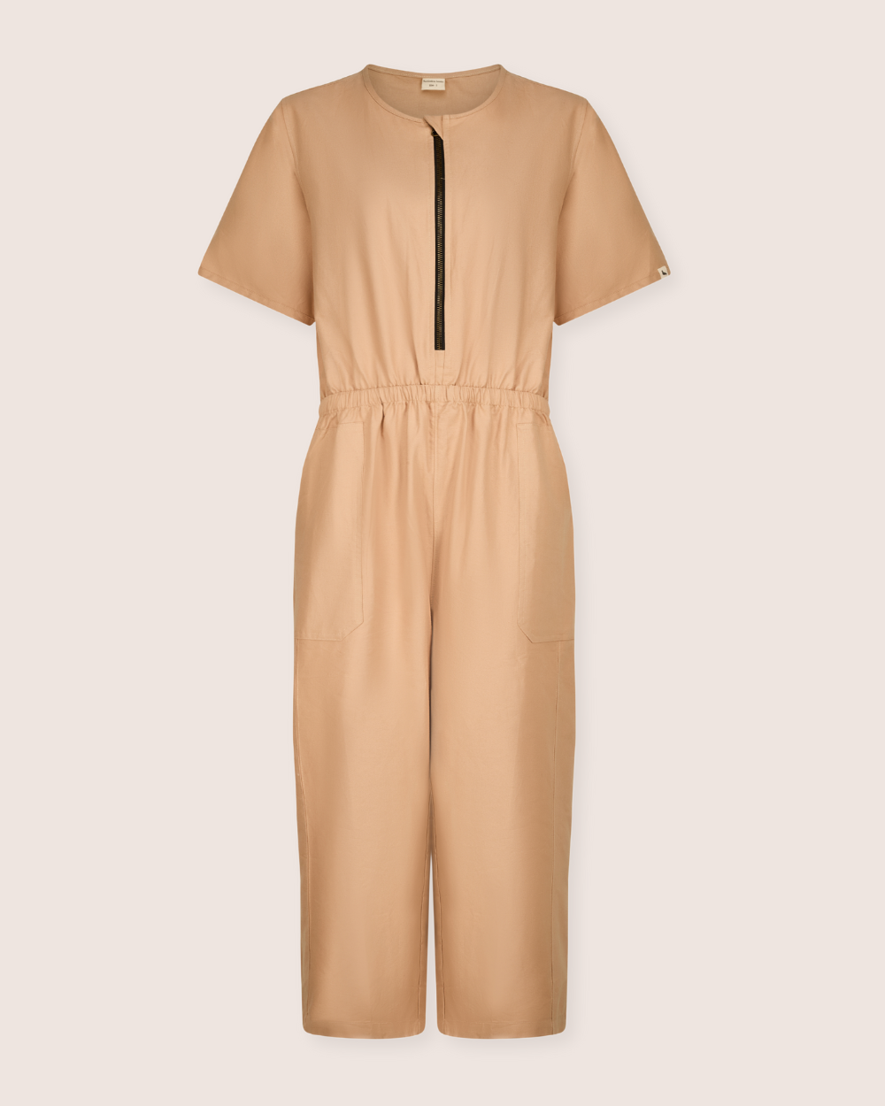 The Ethel Plain Clay Jumpsuit is a beige, short-sleeve outfit with a black front zip and elastic waistband. It includes two large front pockets for easy breastfeeding access and is made from lightweight fabric, ideal for casual wear.