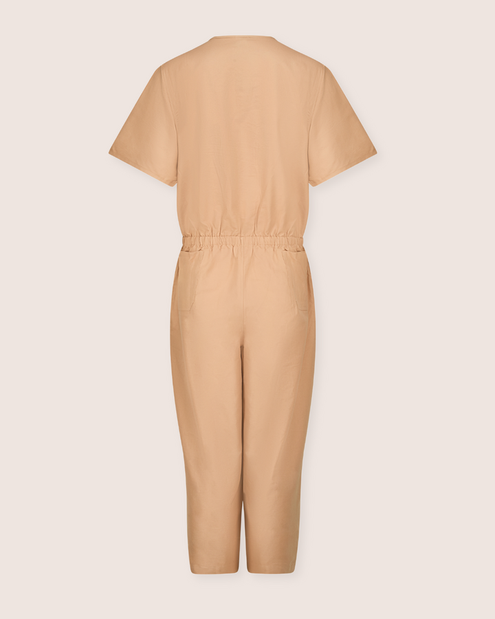 The Ethel Plain Clay Jumpsuit is beige and short-sleeved, made from organic cotton with a cinched waist. Displayed from the back to showcase its solid simplicity against a light background, it features an easy access breastfeeding option for convenience.