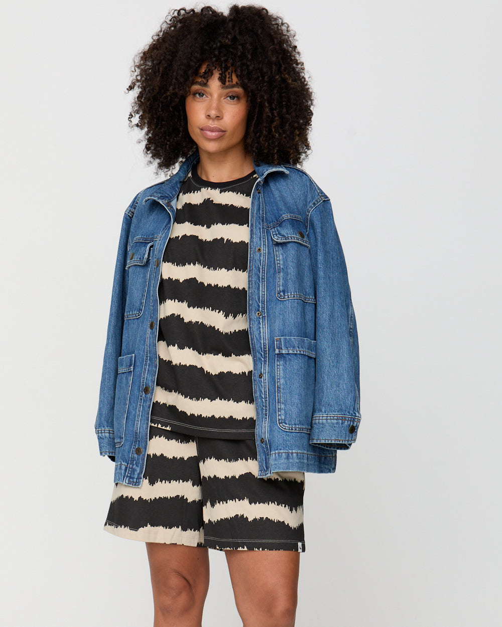 Woman wearing a denim jacket over a black and white striped dress on a plain background