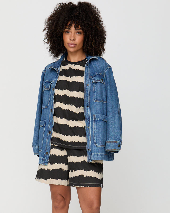 Woman wearing a denim jacket over a black and white striped dress on a plain background