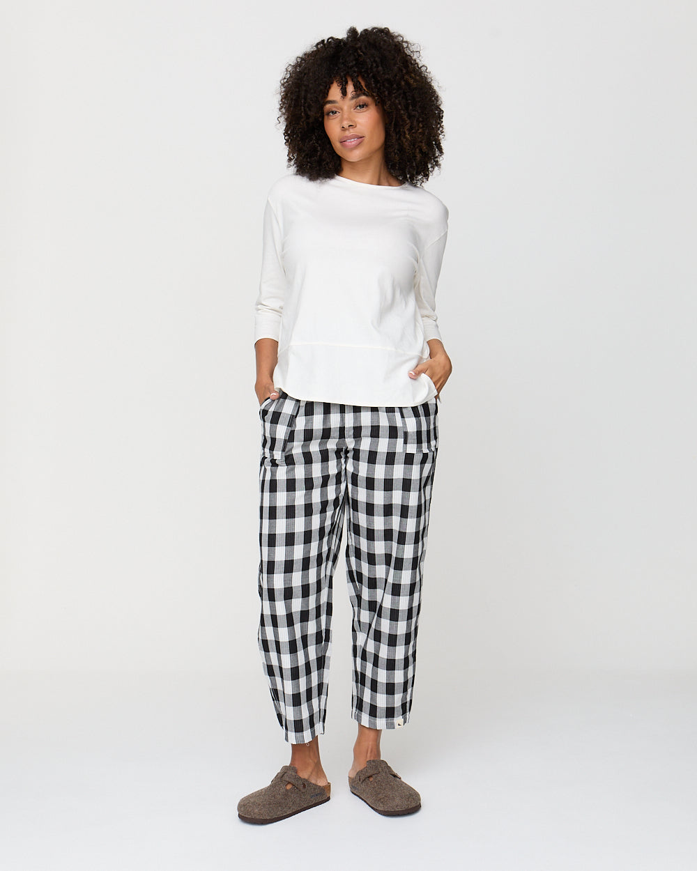 Woman wearing a white top and black and white checkered pants on a white background
