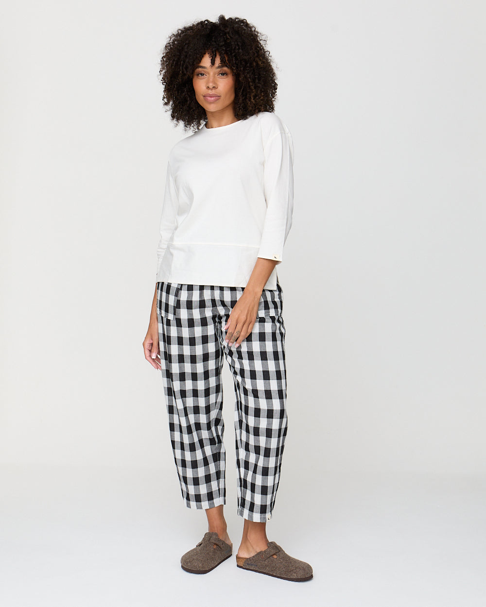 Woman wearing a white top and black and white checkered pants on a white background