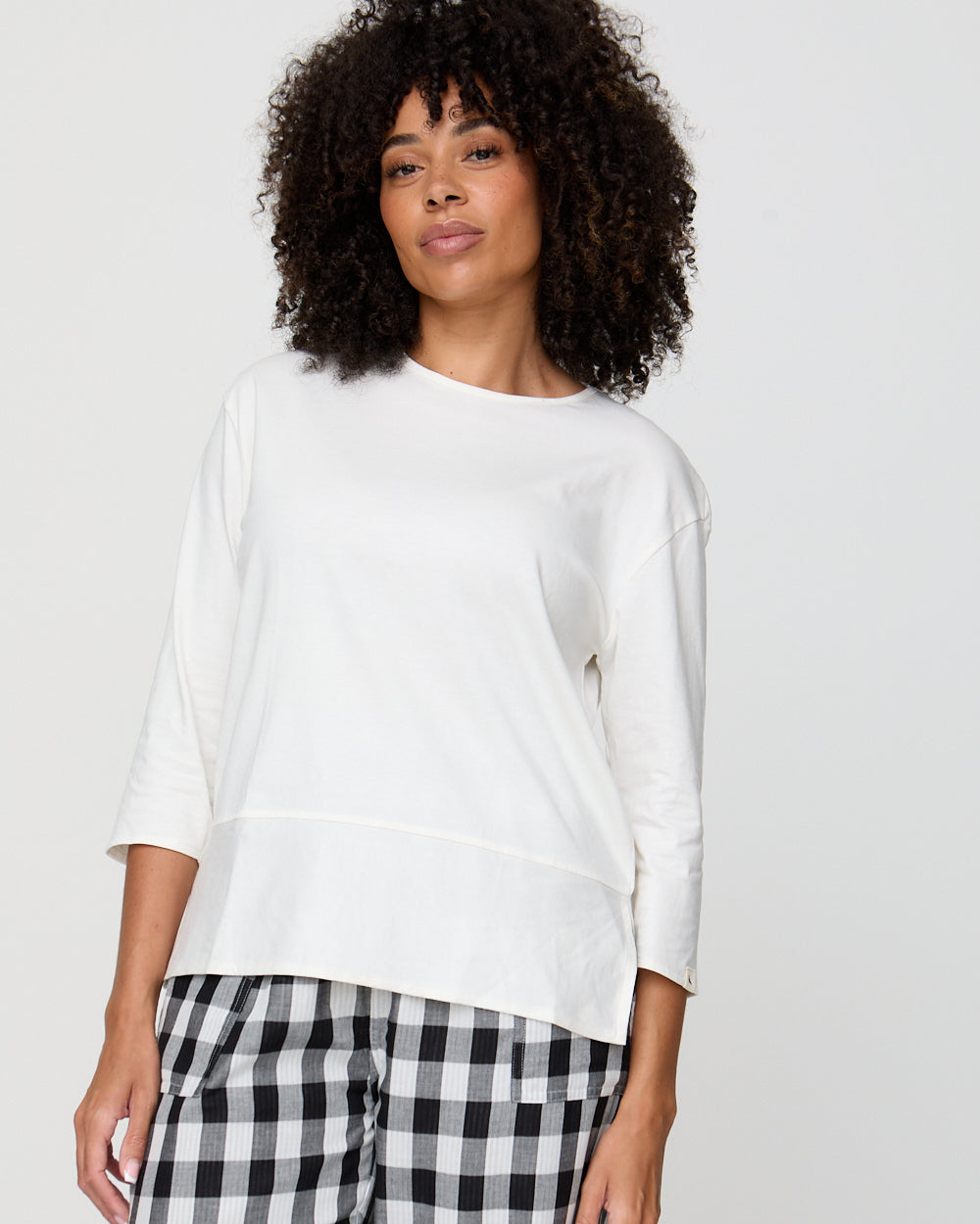 Woman wearing a white top and black and white checkered pants on a plain background