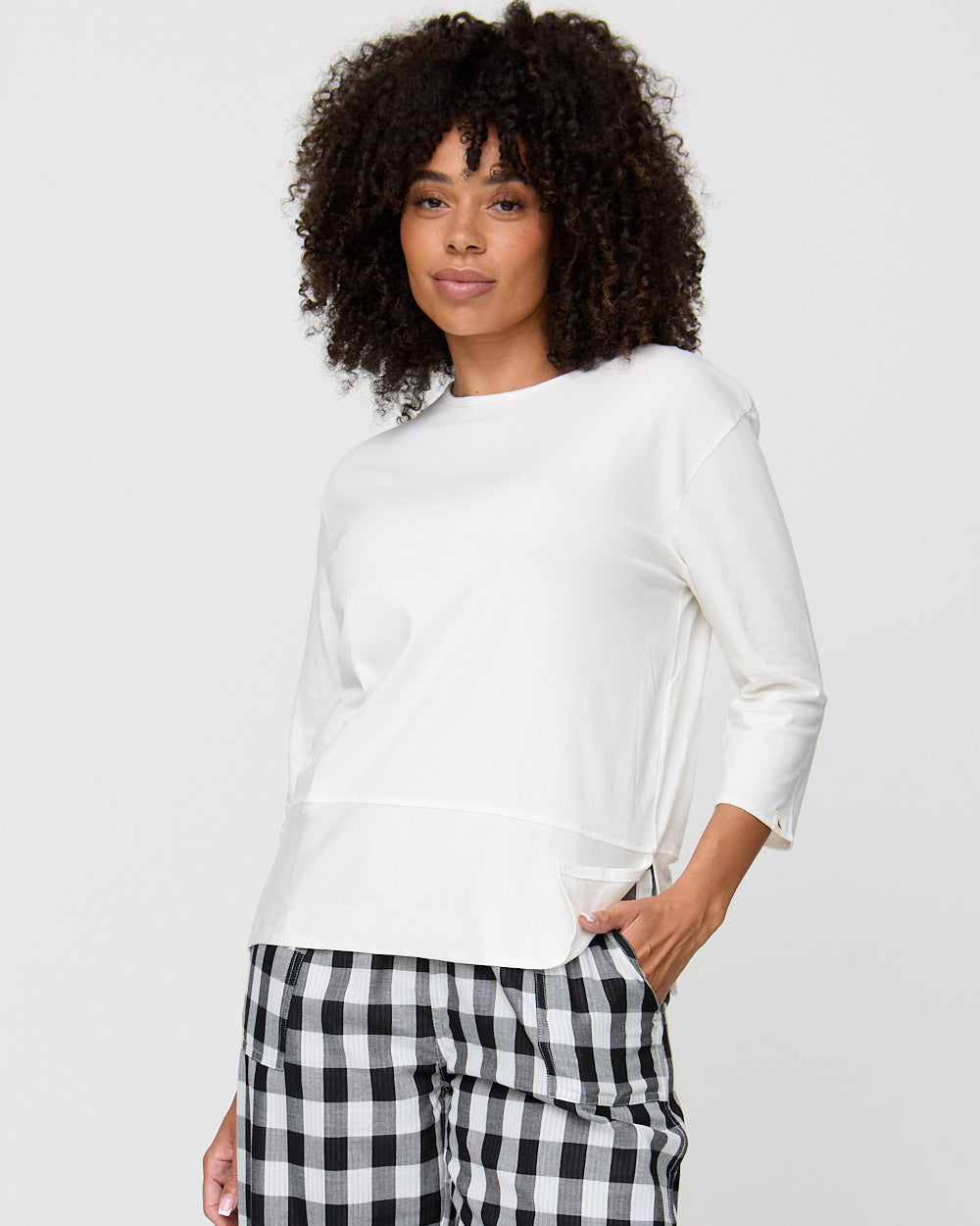 Woman wearing a white sweater and black and white checkered pants on a plain background
