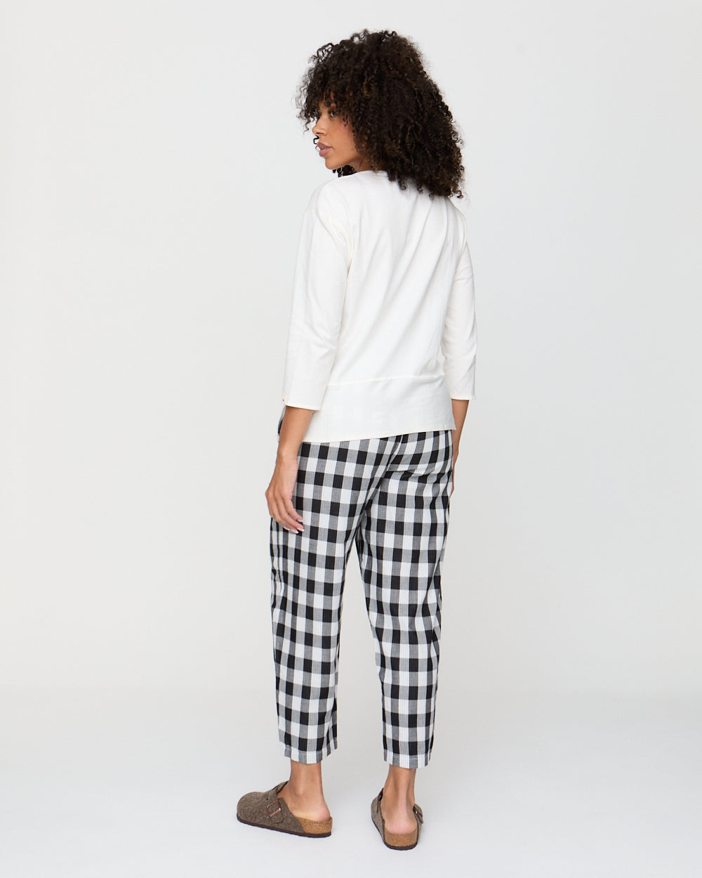 Woman wearing a white top and black and white checkered pants on a plain background