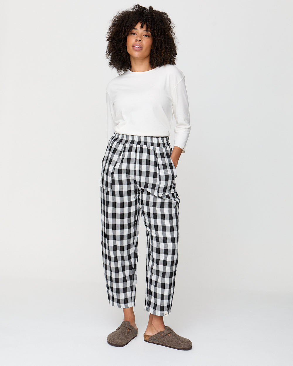 Person wearing a white top and black and white checkered pants on a plain background
