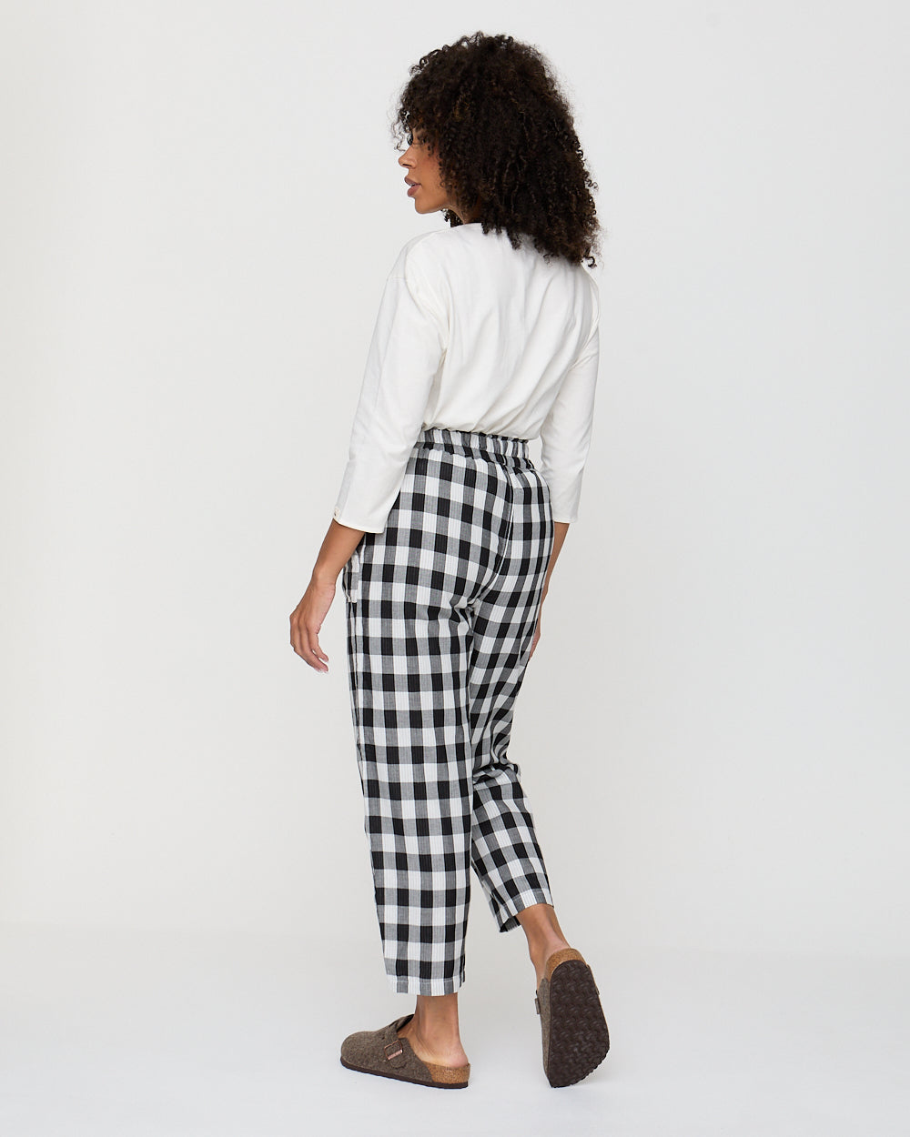 Person wearing a white shirt and black and white checkered pants on a white background