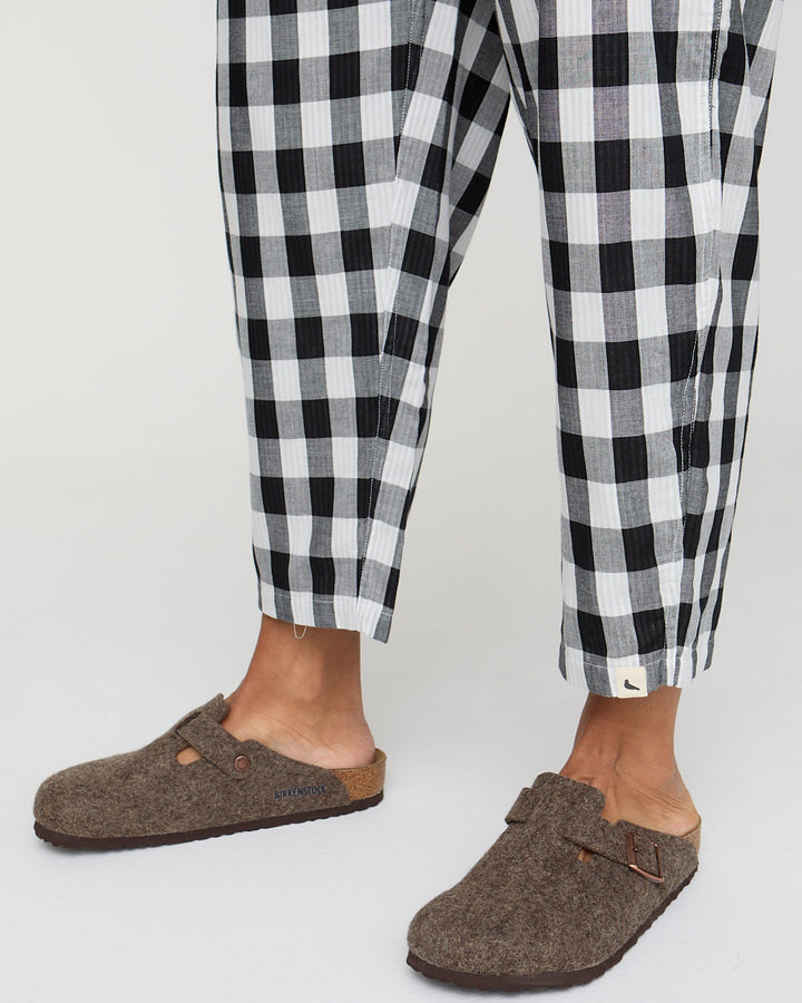 Person wearing black and white checkered pants with brown slippers on a light gray background