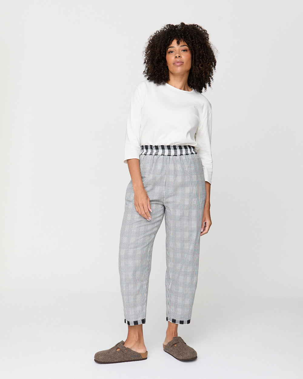 Woman wearing a white sweater and gray checkered pants on a white background