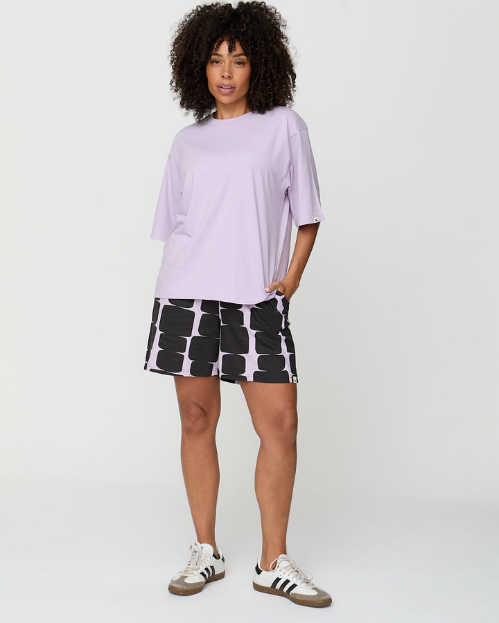 Woman wearing a light purple oversized t-shirt and black and white patterned skirt on a plain background