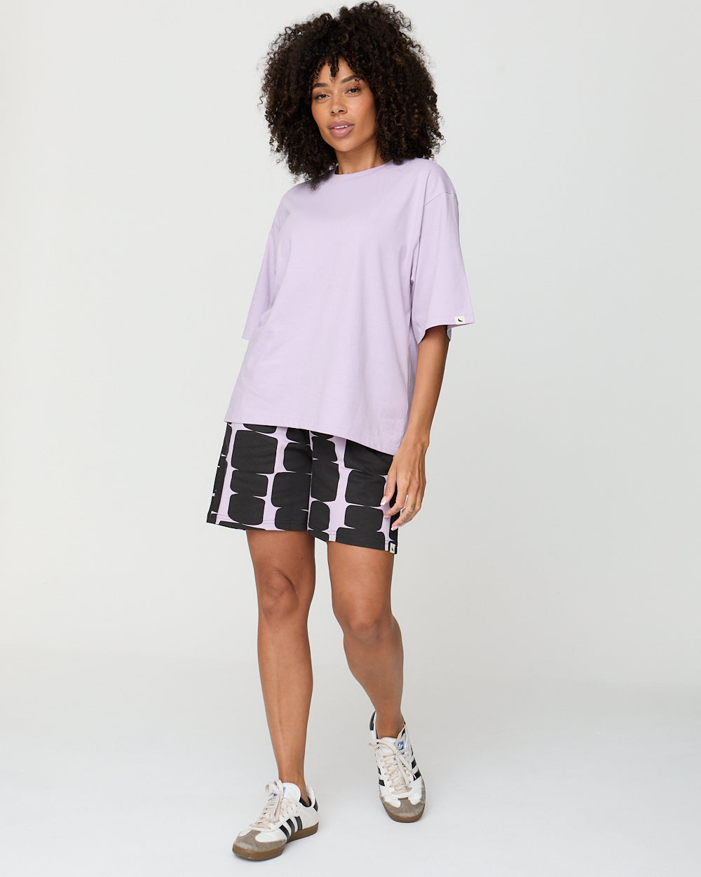 Woman wearing a light purple oversized shirt and black and white patterned shorts on a white background