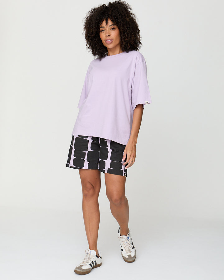 Woman wearing a light purple oversized shirt and black and white patterned shorts on a white background