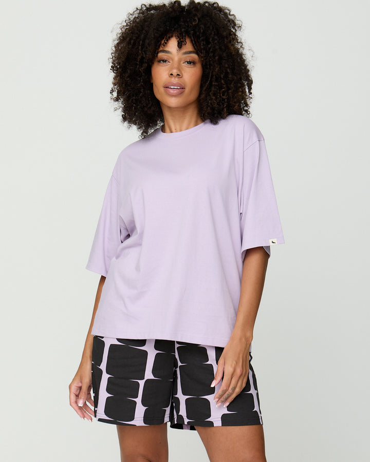 Woman wearing a light purple oversized t-shirt and black patterned shorts on a white background