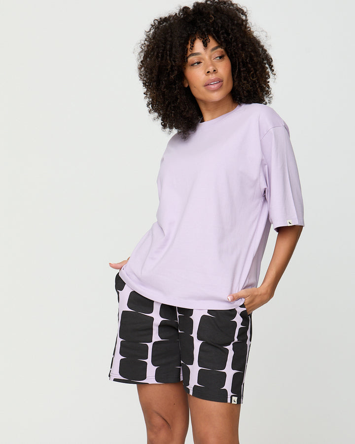 Woman wearing a light purple oversized t-shirt and black and white patterned shorts on a white background