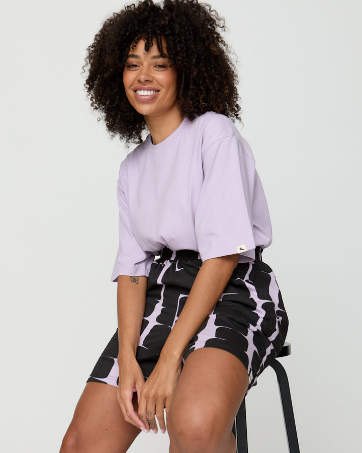 Woman wearing a light purple shirt and black and white patterned shorts on a plain background