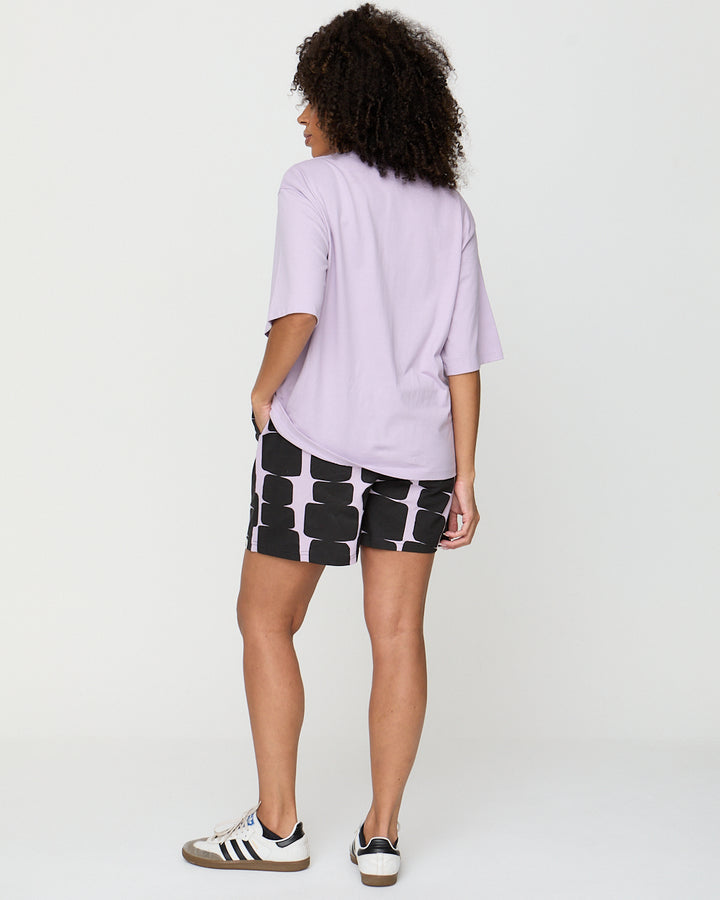 Person wearing a light purple t-shirt and black and white patterned shorts on a plain background