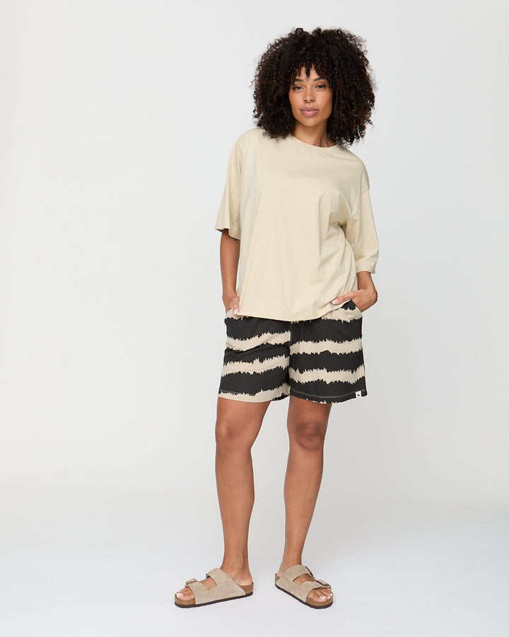Woman wearing a beige top and black and white striped shorts on a white background