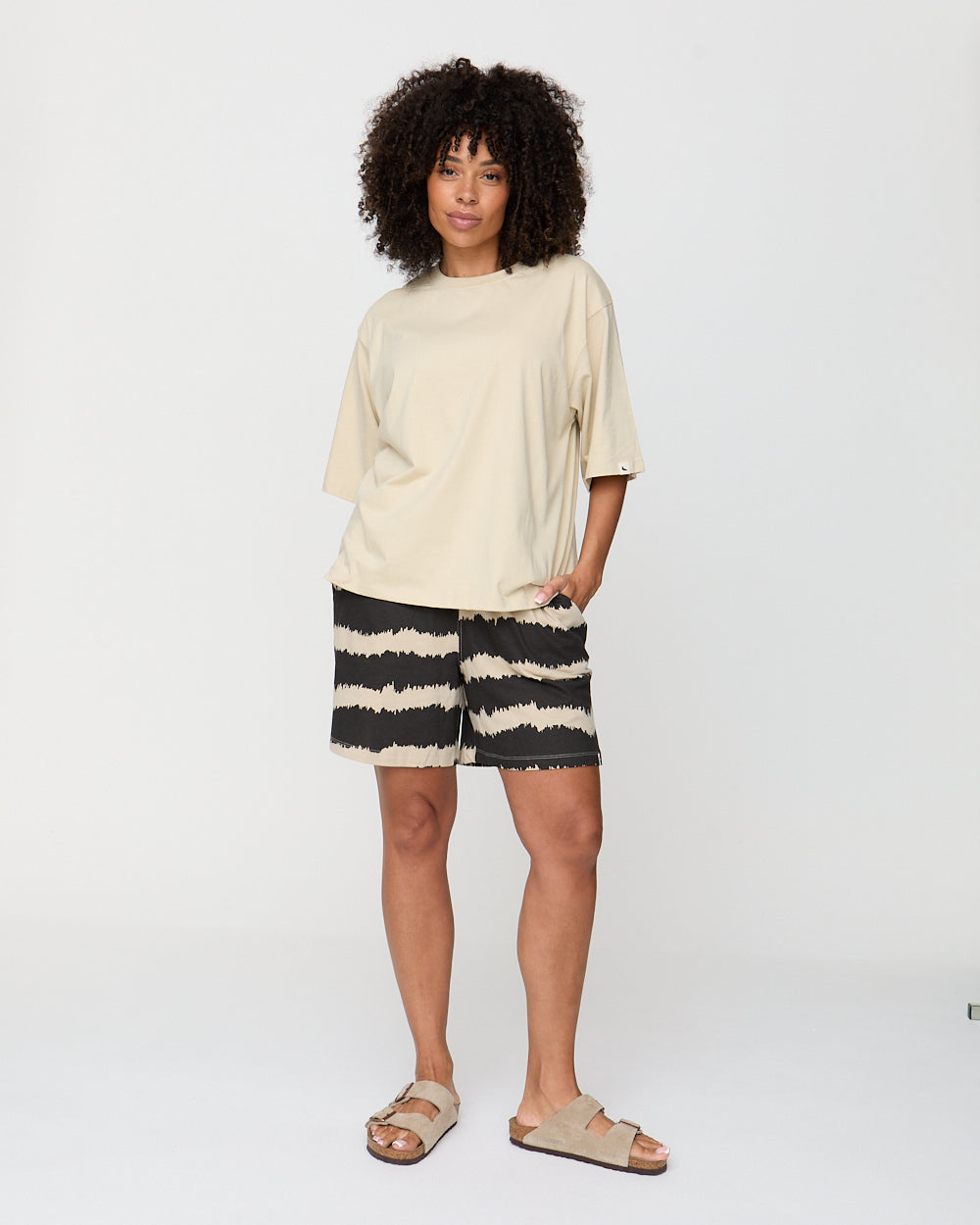Person wearing a beige top and black and white striped shorts on a white background