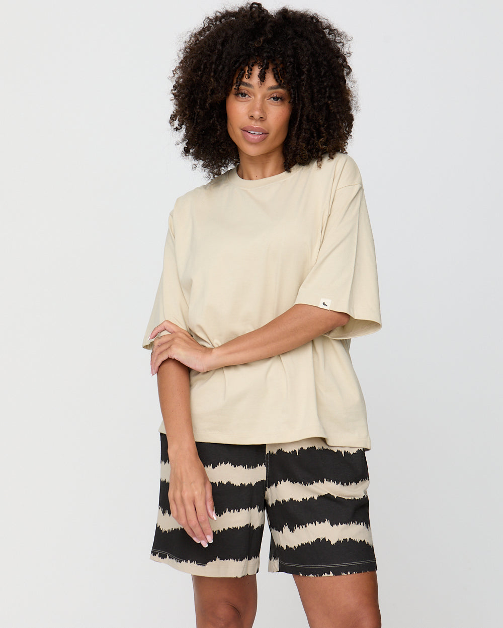 Woman wearing a beige top and black and white striped shorts on a plain background