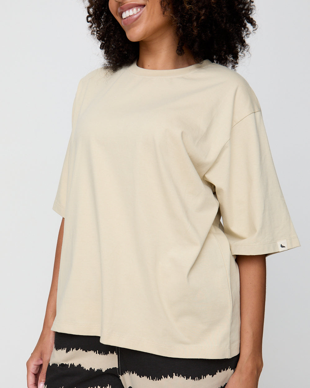 Woman wearing a beige oversized t-shirt against a plain background