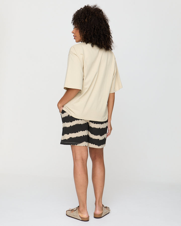 Person wearing a beige oversized shirt and striped shorts on a plain background
