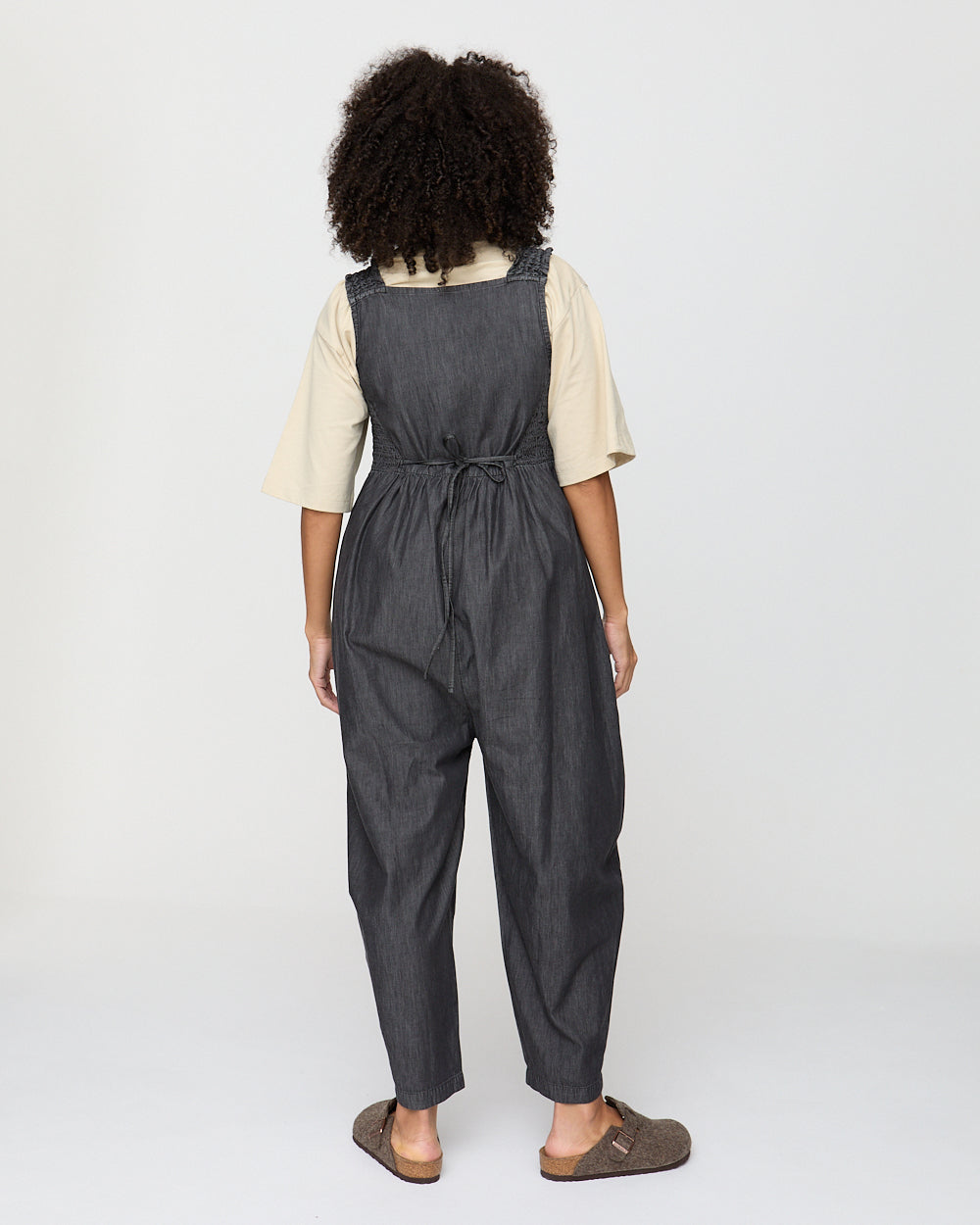 Person wearing a dark denim overalls on a white background