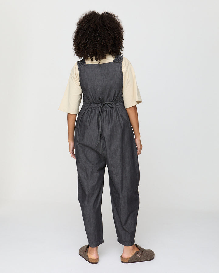 Person wearing a dark denim overalls on a white background