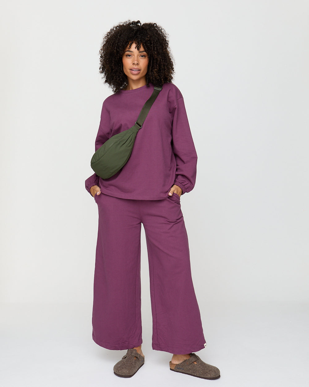 Person wearing a purple outfit with a green bag on a white background