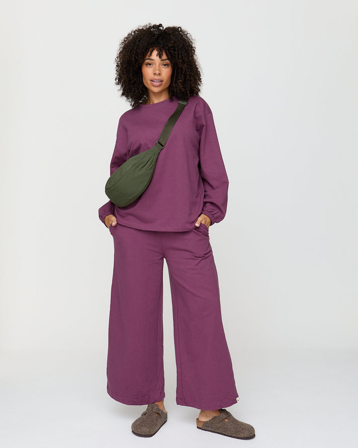 Person wearing a purple outfit with a green bag on a white background