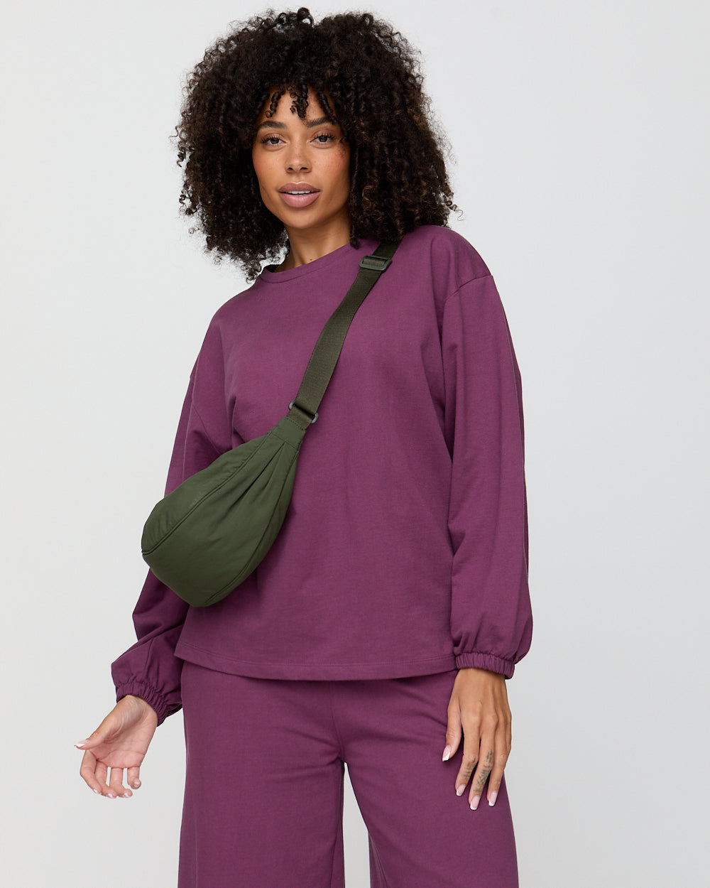 Person wearing a purple outfit with a green bag on a plain background