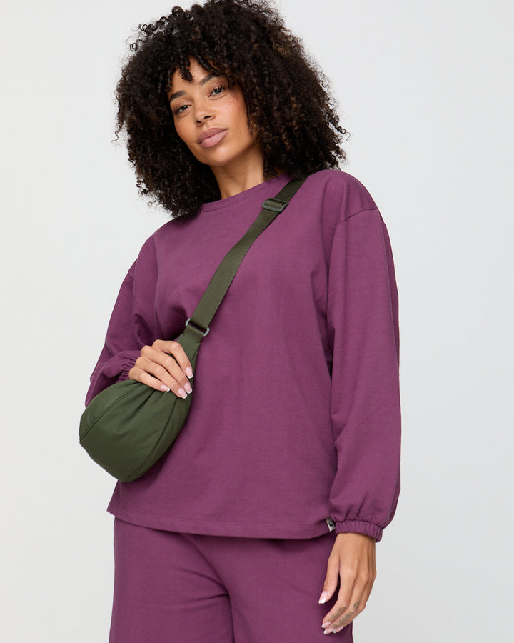 Woman wearing a purple outfit with a green bag against a white background
