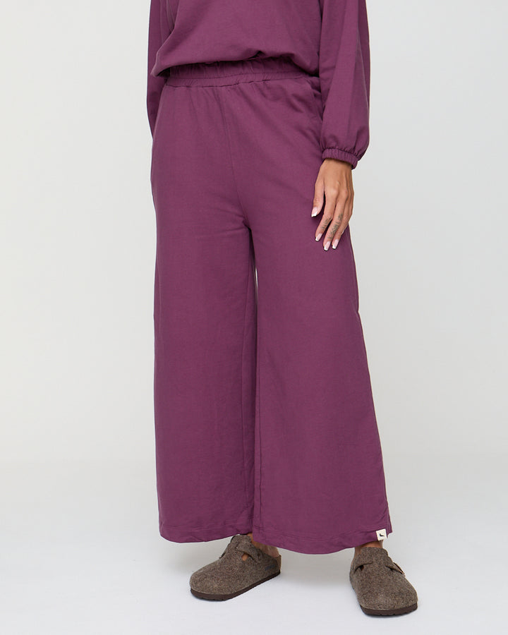 Person wearing a purple outfit with wide-leg pants on a plain background