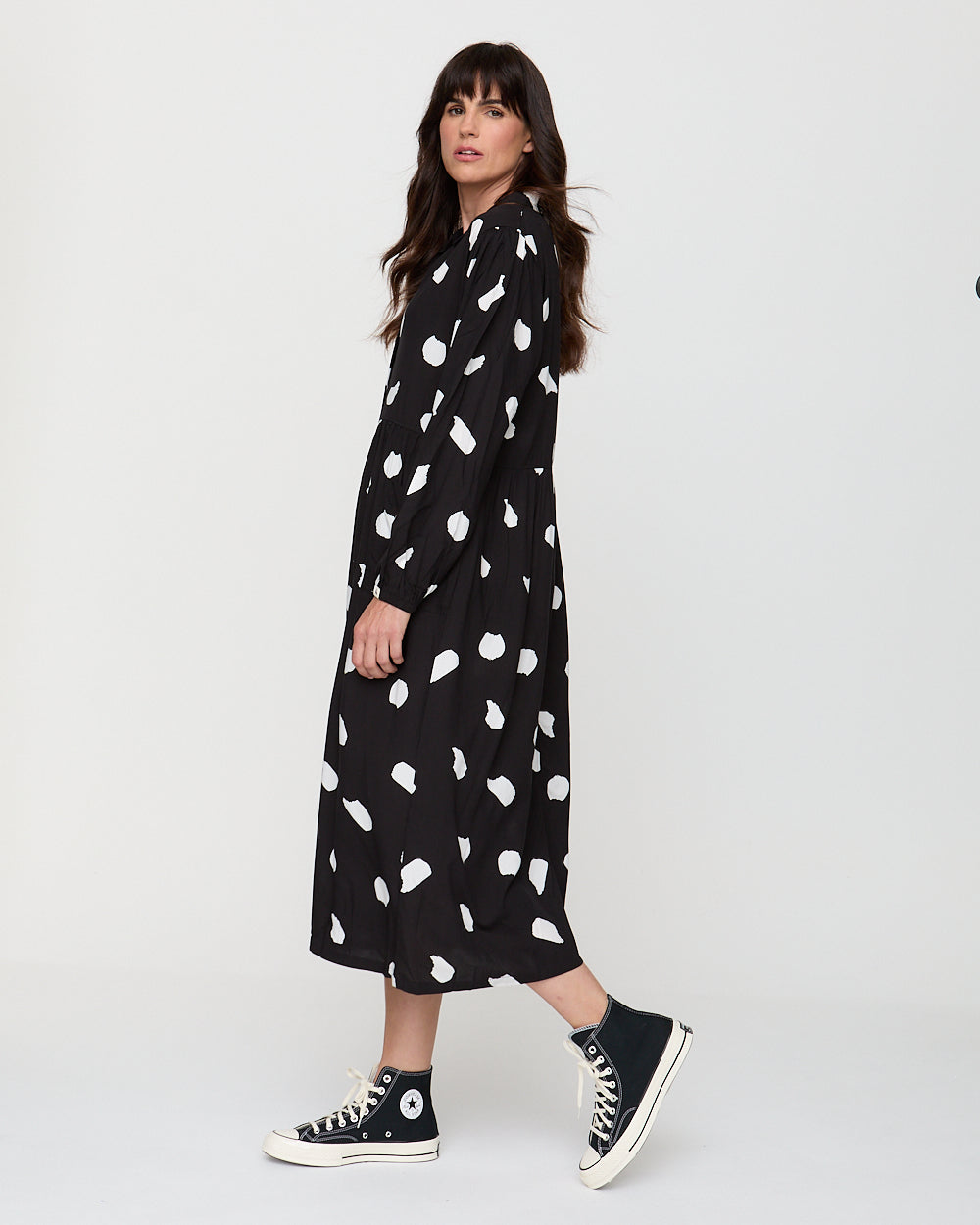 Woman wearing a black dress with white patterns and black sneakers on a white background