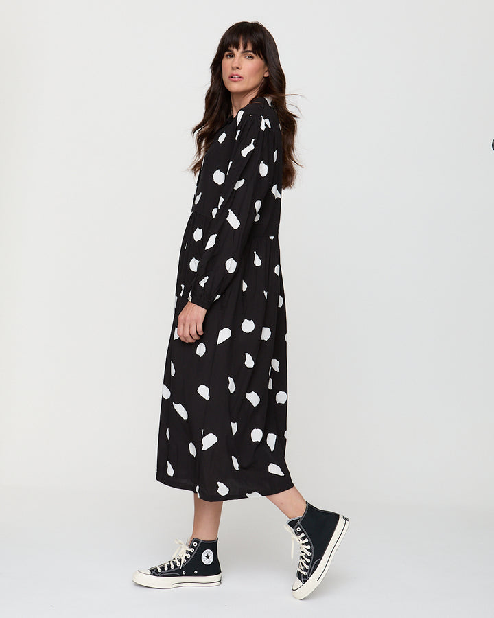 Woman wearing a black dress with white patterns and black sneakers on a white background