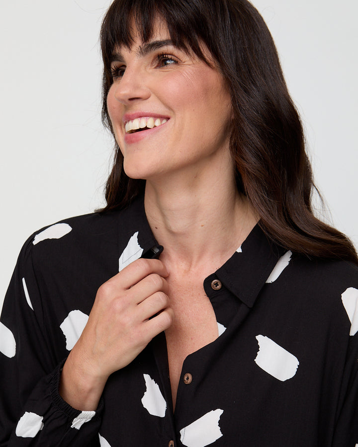 Woman wearing a black shirt with white polka dots, smiling against a plain background